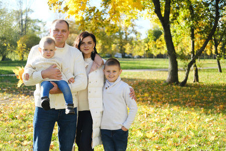 A happy family of four spend time in the autumn park. Family smiling and looking at the camera....