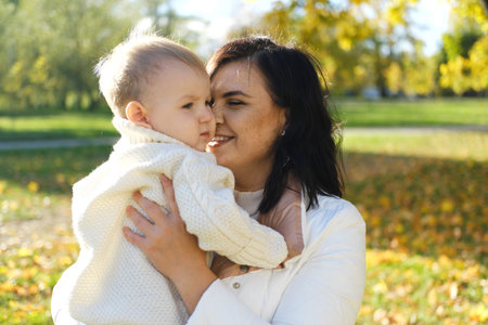 Mother and son walking in autumn park outdoor. Woman holding toddler boy on hands. Family of two....