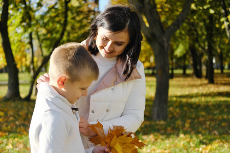 Mother with son on a walk in the autumn park. Woman talking to her son and smiling. Horizontal photoの写真素材