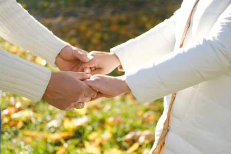 A man and a woman stand opposite each other and hold hands in the autumn park. Hands shot close up. Horizontal photoの写真素材
