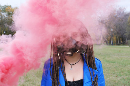 Portrait of a Woman in a blue jacket and dreadlocks in a gas mask with spikes. woman standing in smoke. Horizontal photoの写真素材