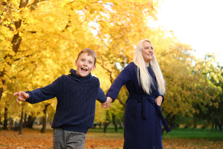 Mother and son walk in the autumn park holding hands. Horizontal photoの写真素材