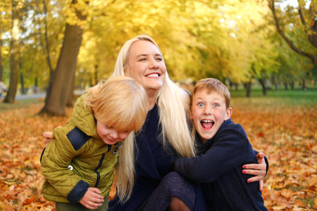 Happy mother is hugged by two sons. Family spending free time together in autumn park. Horizontal...