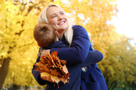 The boy gave his mother a bouquet of autumn leaves and his mother hugs him. Horizontal photoの写真素材