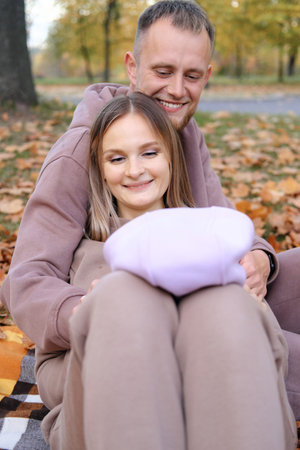 Young parents sit on a plaid with a newborn baby in the autumn park. The child lies on the lap of the mother, the parents play with the child. Vertical photoの写真素材