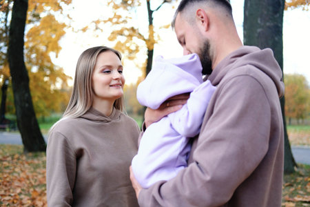 Young mother and father are walking with a newborn baby in the autumn park. Parents look at the child with tenderness. Horizontal photoの写真素材