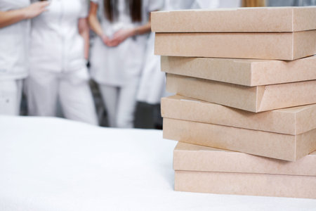 Stacked catering boxes with appetizers on a table in the foreground, with a group of medical...