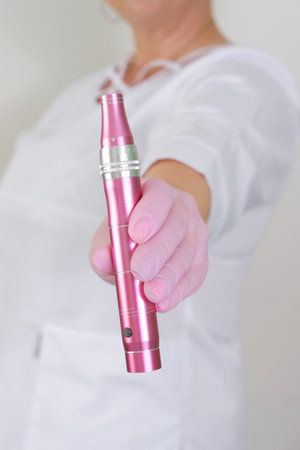 A cosmetologist in a white coat is holding a dermapen, a specialized device used for microneedling skin treatment procedures.の写真素材