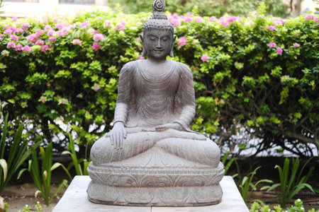 A classic stone Buddha statue creates a focal point of calm and sophistication against a backdrop of a well-groomed hedge.の写真素材