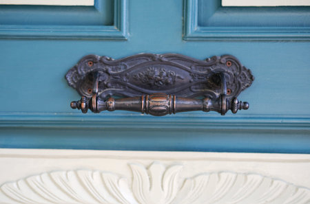 Close-up of a decorative vintage door handle on a carved blue wooden door with white detailing