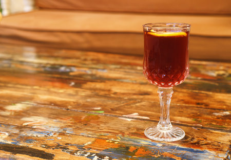 A richly hued beverage in a faceted crystal glass topped with a fresh lemon slice, presented on a vibrantly painted wooden tableの写真素材