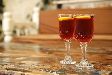 Two crystal glasses filled with a dark amber liquid and garnished with orange slices sit on a rustic wooden table.の写真素材