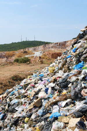 A garbage dump site stretching towards green trees and distant antennas, illustrating an...
