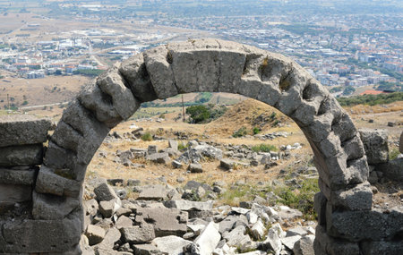 Ancient stone arch with a view of the city and surrounding landscape. The foreground shows ruins and rocks.の写真素材