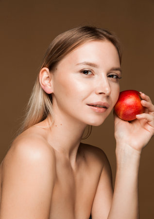 A close-up portrait of a beautiful blonde woman holding a red apple against her cheek, showing healthy, glowing skin and a serene expression.の写真素材