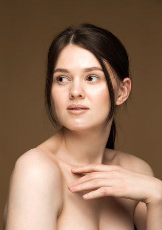 Portrait of a young brunette Caucasian woman with clear skin and bare shoulders, emphasizing youthful skin and collagen production. Brown background.の写真素材
