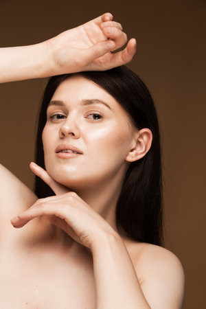 Close-up of brunette woman after face exercises, emphasizing her healthy skin against a brown backgroundの写真素材