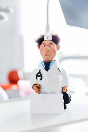 Doctor figurine in medical uniform standing on dental equipment in a brightly lit dentist's office. Dental chair and supplies are visible in the background.の写真素材