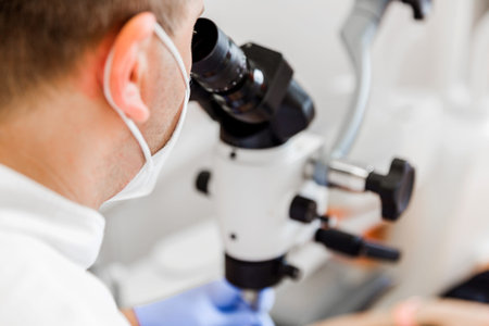 Dentist in mask using a microscope to examine a patient's teeth during a procedure in a modern...