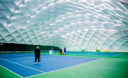 An indoor tennis court with a blue and green surface, featuring multiple players practicing. The court is inside a dome with bright lights.の写真素材