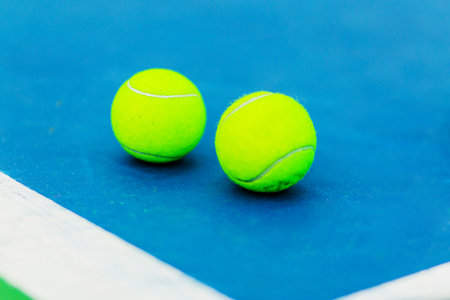 Two bright yellow tennis balls resting on the corner of a blue tennis court.の写真素材