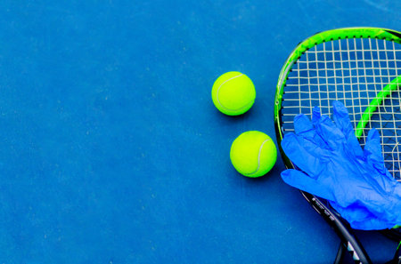 Top view of tennis rackets, balls, and blue protective gloves on a blue tennis court. The empty space is ideal for adding text, making it suitable for banner use. The gloves emphasize protection against bacteria and infections.の写真素材