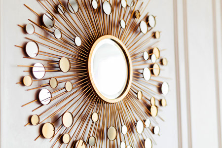 A stylish decorative mirror with a gold frame, designed with radiating elements, mounted on a light-colored wall.の写真素材