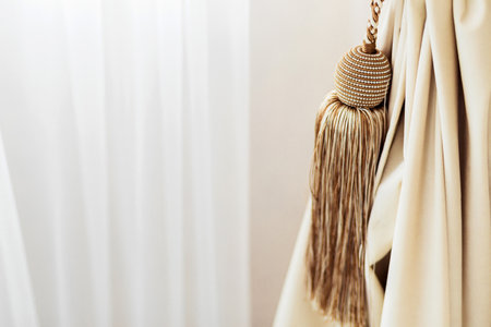 Close-up of an elegant beige curtain tieback with a decorative tassel, adding a touch of sophistication to the room.の写真素材