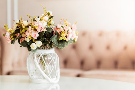 Elegant floral arrangement in a glass vase with a white rope accent. Soft background with a beige sofa.の写真素材