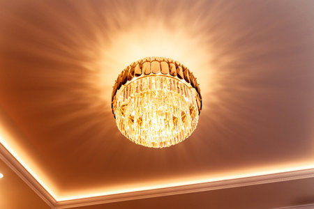 A luxurious crystal chandelier casting warm, elegant light patterns on the ceiling, creating a sophisticated ambiance.の写真素材