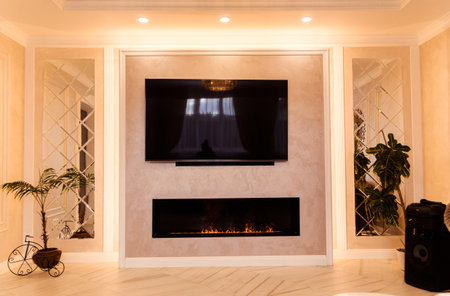 A modern living room with evening lighting, featuring a wall-mounted TV, an elegant fireplace, and ceiling LED lights.の写真素材