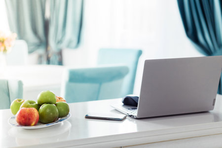 A modern home office setup with a laptop, a plate of apples, and elegant blue curtains in a bright room for a productive atmosphere.の写真素材