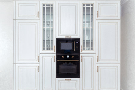 Elegant white kitchen cabinetry with built-in black appliances. Sophisticated kitchen interior with a blend of classic and modern design elements.の写真素材