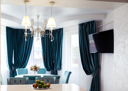 Dining room with elegant lighting fixtures, teal curtains, and a round table set.の写真素材