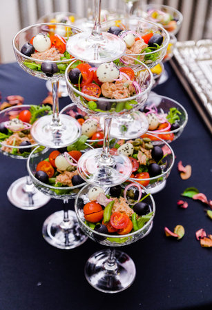 Pyramid of glasses filled with vibrant salads, featuring tomatoes, olives, and greens on a dark...