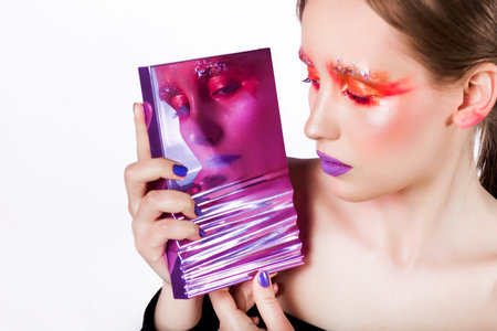A woman with creative makeup and vibrant purple lipstick holds a reflective surface, showing her striking look against a white background.の写真素材
