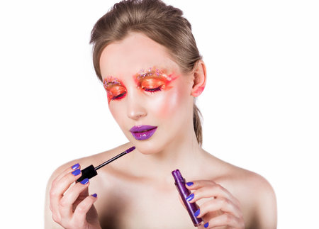 Woman applying bold purple lipstick with vibrant, creative makeup. Close-up on white background showcasing a unique, fashionable look.の写真素材