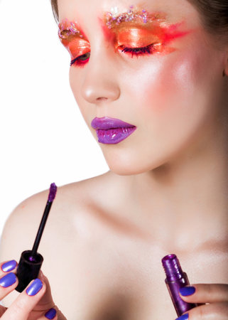 Woman applying vibrant purple lip gloss with creative makeup. Close-up on white background, showcasing stylish, artistic look.の写真素材