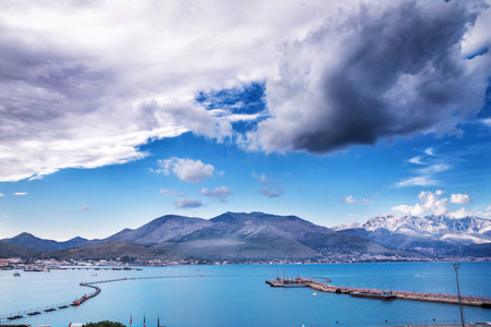 Stunning view of a coastal seaport in Italy with mountains in the background and dramatic clouds in the sky.の写真素材