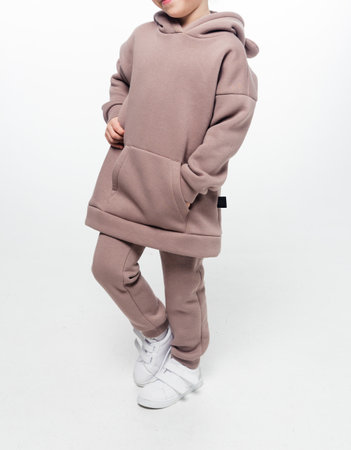 A young girl in a brown hoodie and matching pants set, posing against a white background. Full outfit visible.の写真素材