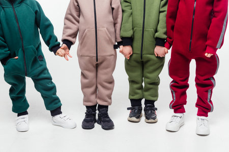 Four kids in green, brown, olive, and red jumpsuits hold hands, showcasing their outfits. Horizontal photo.の写真素材