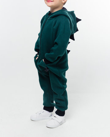 A child in a green jumpsuit featuring black dinosaur spikes, standing sideways with hands in pockets. Vertical photo.の写真素材