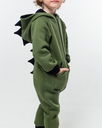 A child wearing a green jumpsuit with black dinosaur spikes, standing sideways with hands in pockets. Vertical photo.の写真素材