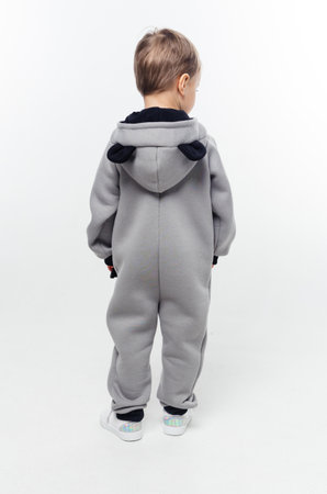A boy in a gray jumpsuit with a hood, standing with his back to the camera. Vertical photo.の写真素材