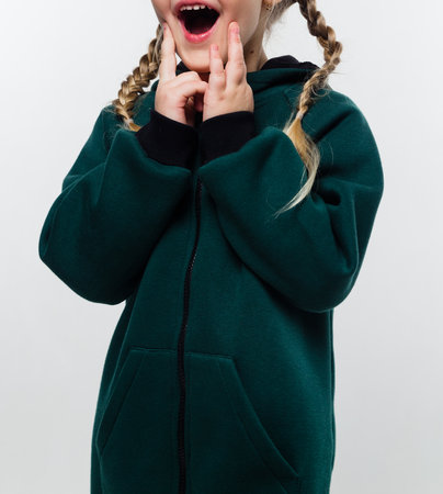 A young girl wearing a green hoodie, with braided hair, expressing surprise with her mouth open and hands near her face.の写真素材