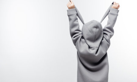 A young child in a gray hoodie with bunny ears, holding the ears up against a white background. Banner with copy spaceの写真素材