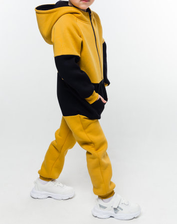 A young child wearing a yellow and black hoodie, walking sideways against a white background. Vertical photo.の写真素材