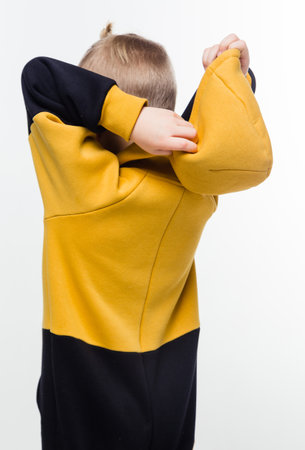 A young child in a yellow and black hoodie pulling the hood over their head against a white background. Vertical photoの写真素材