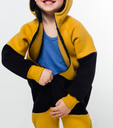 A young child in a yellow and black hoodie, smiling while pulling the zipper, revealing a blue shirt underneath, against a white background. Vertical photo.の写真素材