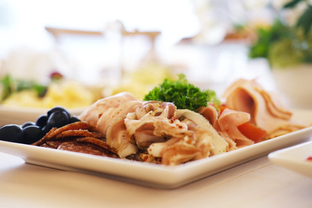 Assorted cured meats, olives, and fresh greens are elegantly arranged on a white plate, highlighting the artistry of gourmet food presentation and culinary creativityの写真素材